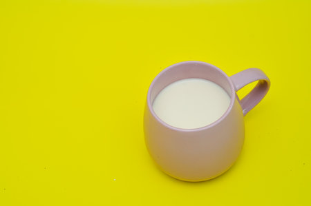 Milk in a pink cup on a yellow background with copy spaceの写真素材