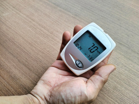 Close up of male hand holding digital glucometer on wooden background