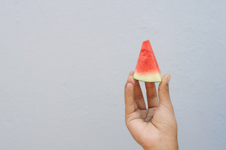 Watermelon slice in hand on white wall background, selective focus.の写真素材