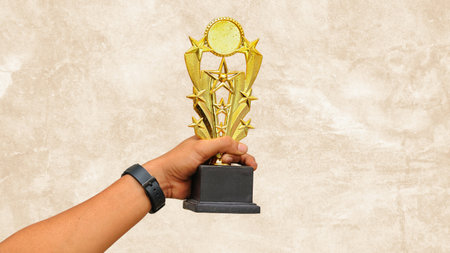 Hand holding gold award cup on grunge wall background with copy space