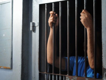Prisoner with his hands behind the bars of a prison cellの写真素材