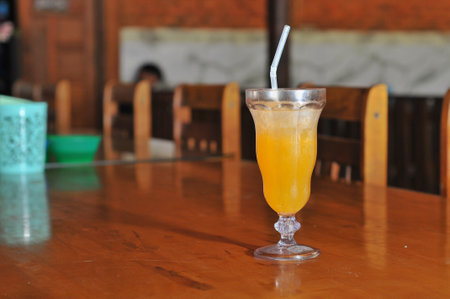 Orange juice in a glass with straw on the wooden table in cafeの写真素材