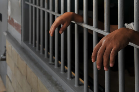 Close up of a man hands behind the bars of a prison cellの写真素材