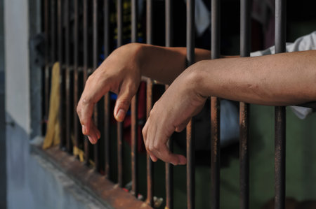 Hand of a man holding a metal cage in a jail, close upの写真素材