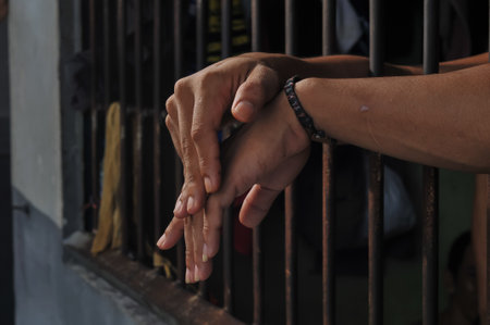 Hands of a man and a woman holding hands on a prison cellの写真素材