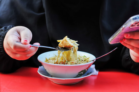 Woman eating spaghetti in a restaurant, closeup of hands with mobile phoneの写真素材
