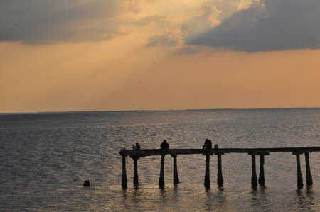 silhouette of people sitting on a wooden bridge over the seaの写真素材