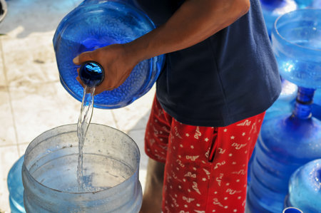 Thai man pouring water from a big blue bottle into a small bowlの写真素材