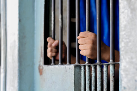 Close-up of an inmateâs hand holding prison bars in a dark cell. Concept of imprisonment, punishment, confinement, and criminal justice.の写真素材