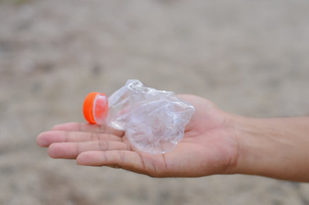 Human hand holding plastic bottle on the beach. Pollution concept.の写真素材