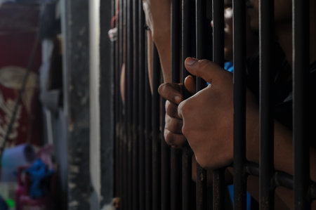 Close-up of an inmateâ€™s hand holding prison bars in a dark cell. Concept of imprisonment,...