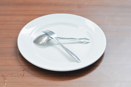 Empty plate with spoon and fork on wooden table, shallow depth of fieldの写真素材