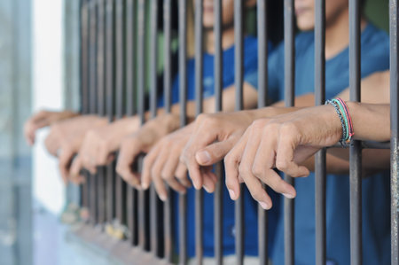 Prisoners hands behind bars. Selective focus and shallow depth of field.の写真素材
