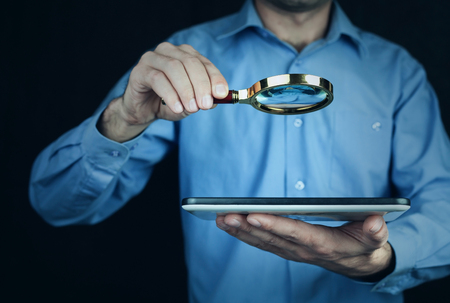 Man holding magnifying glass and tablet.の写真素材