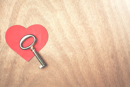 Key and paper heart on a wood background.
