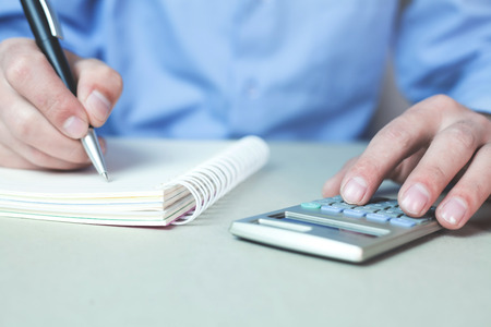 Man using calculator and writing on a notepad.の写真素材