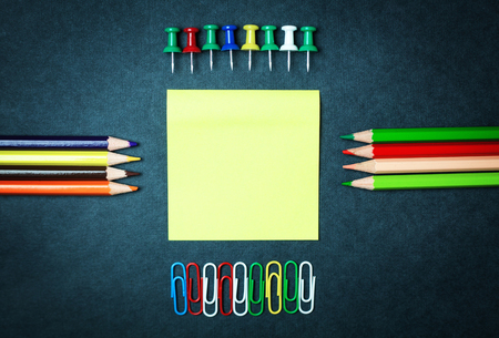 Yellow sticky note with colored paper clips and push pins on a blue background.の写真素材