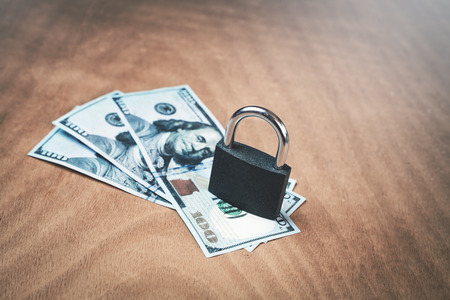 Padlock with hundred dollars on a wood background.