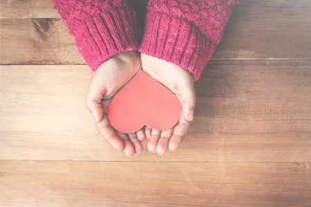 Red heart in hands on a wood background.の写真素材