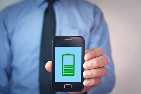 Man showing phone with green battery icon on screen.の写真素材