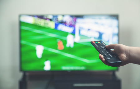Watching football match on tv with remote controller.の写真素材