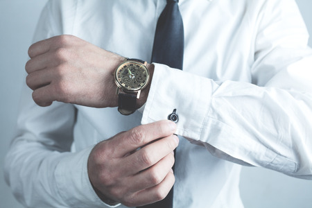 Businessman fastening buttons on shirt sleeve.