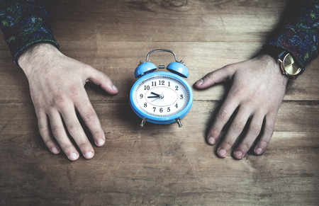 Hands holding blue alarm clock on wooden table.