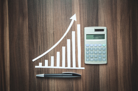 Paper growth graph with calculator and pen on wood background.