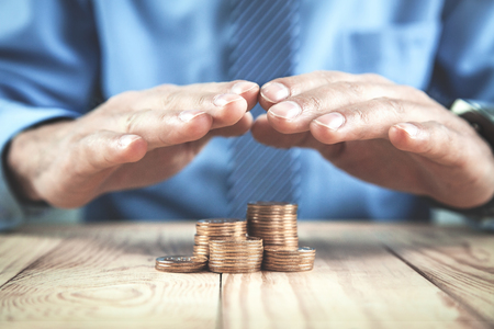 Businessman protect golden coins on wood table. Financial safety conceptの写真素材