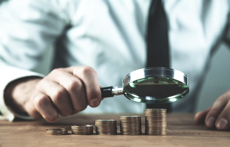 Man analyzing coin stacks with magnifying glass.の写真素材