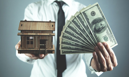 Real estate agent holding wooden house and hundred dollars. Real estate concept