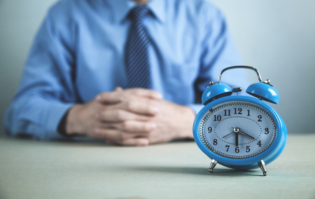 Caucasian businessman sitting at desk with alarm clock. Business conceptの写真素材