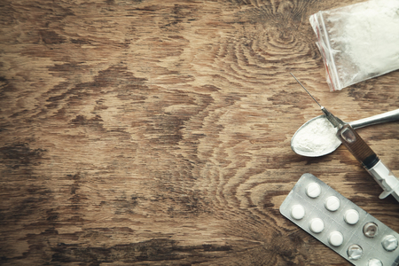 Heroin syringe, spoon, tablets and plastic packet on wooden background. Drug conceptの写真素材