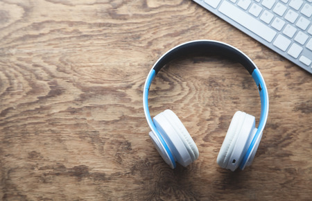 White wireless headphones and computer keyboard on wooden desk.の写真素材