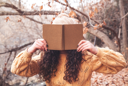 Girl covering her face with book in autumn park.の写真素材