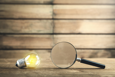 Magnifying glass with light bulb on a wooden background. Concept of creativity, idea, businessの写真素材