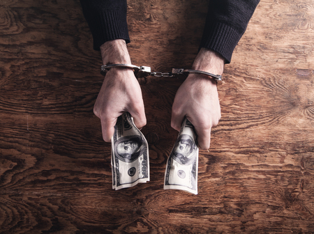 Hands in handcuffs holding dollar banknotes. Corruption