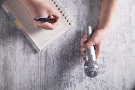 Hands holding microphone and writing on notepad.の写真素材
