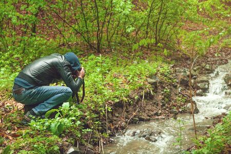 Man taking photo. Water river in the forest.
