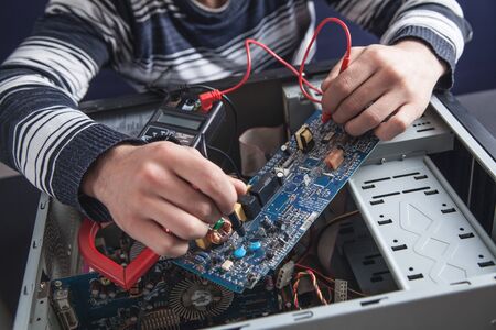Man checking computer with a multimeter.