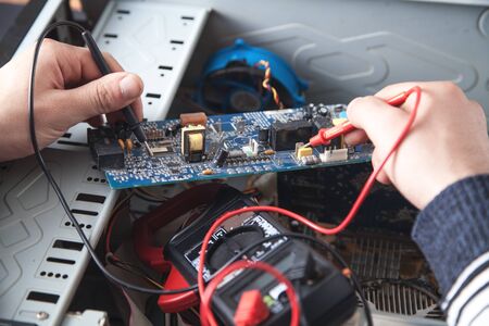 Man checking computer with a multimeter.