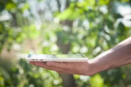 Male hand holding white digital tablet in nature.の写真素材