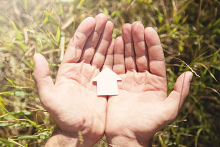 Male hands holding paper house model in nature.の写真素材
