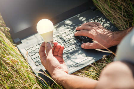 Man holding light bulb and using laptop computer in nature.の写真素材