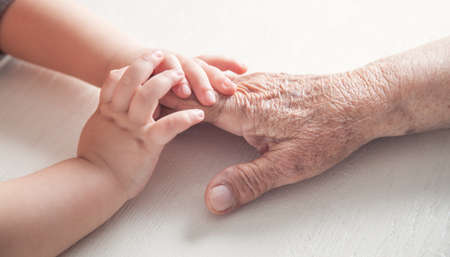 Elderly woman and a kid hands together.