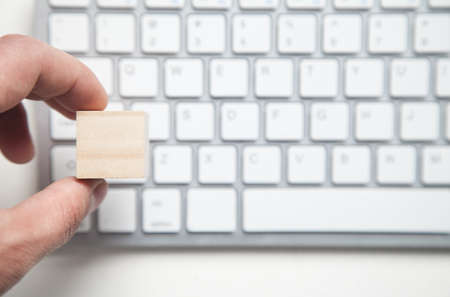Male hand holding wooden blank cube on computer keyboard.
