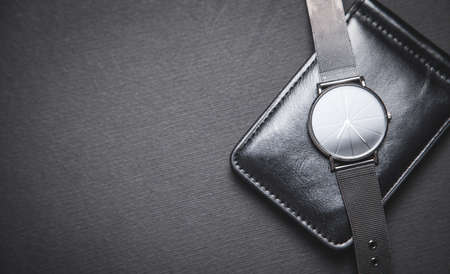 Wristwatch and wallet on the black background.
