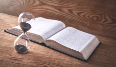 Hourglass with book on wooden table.の写真素材