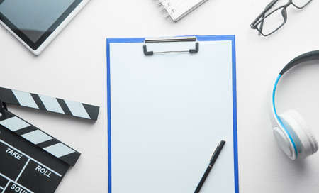 Movie clapper, clipboard, headphones and other objects on white desk.の写真素材