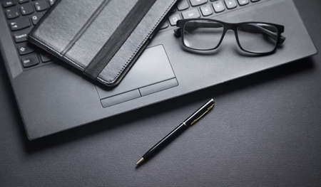 Laptop, pen and glasses on the black background.
